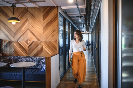 Cheerful Young Businesswoman Walking in Office with Coffee